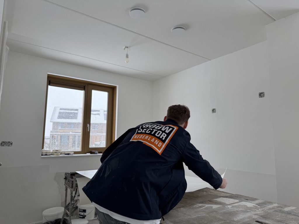 Vakman van Bouwsector Nederland aan het werk bij de plaktafel in een kale kamer met raam
