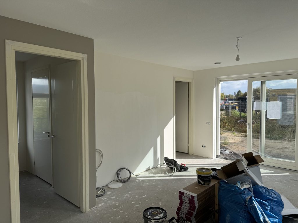 Woonkamer tijdens de afwerking, met kale wanden en gereedschap en materiaal op de vloer
