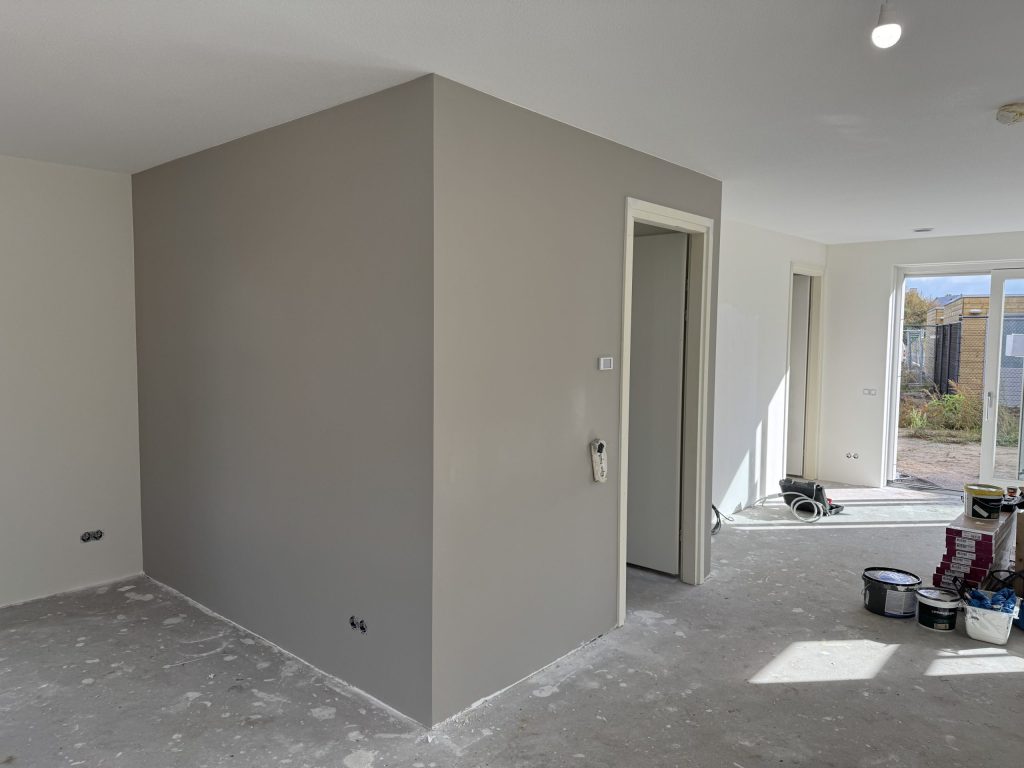 Nieuwbouwkamer met een vrijstaande wand in een grijze tint en verfemmers op de afgedekte vloer