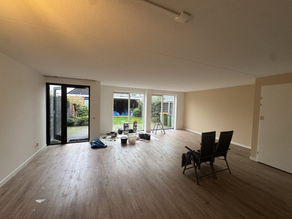 Ruime woonkamer met lichte wanden, een houten vloer en tuindeuren, tijdens de afwerking